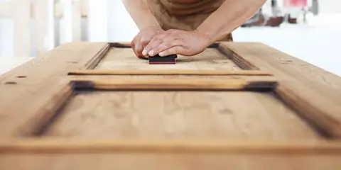 Handwerker schleift Holztür in der Werkstatt – Sanierung und Aufarbeitung